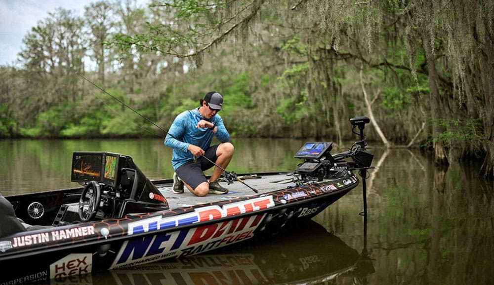 Джастин Хамнер разговаривает по своим смарт-часам quatix® 8 на лодке, держа в руке удочку.